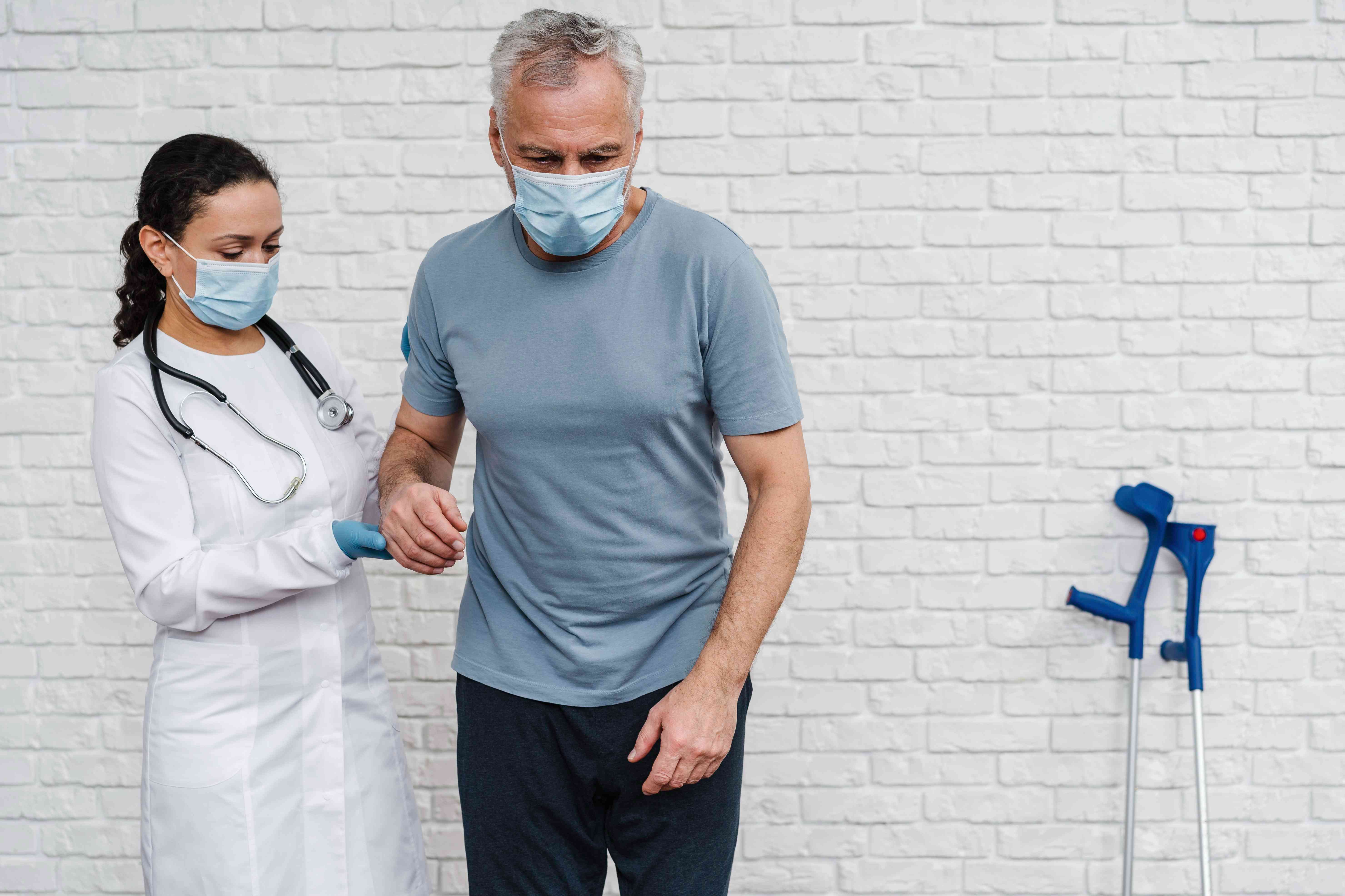 Female doctor assisting an elderly male patient with walking during rehabilitation.